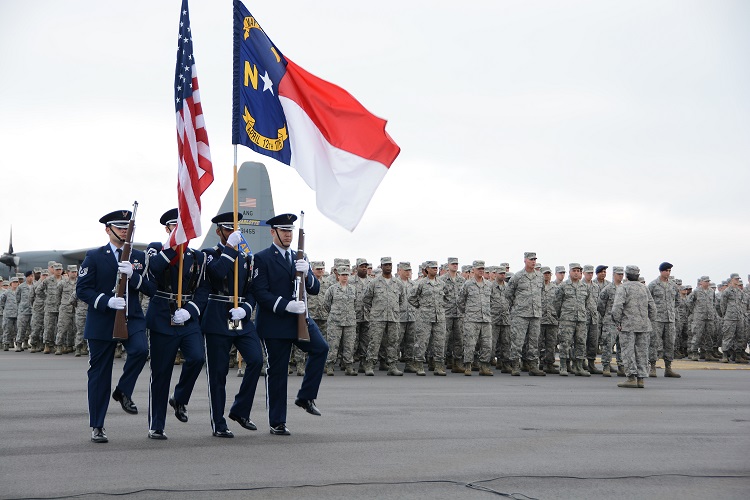 Image of Airmen on the flightline during a ramp formation. The color guard is holding the U.S. Flag and the North Carolina Flag. A C-130 is in the background. 