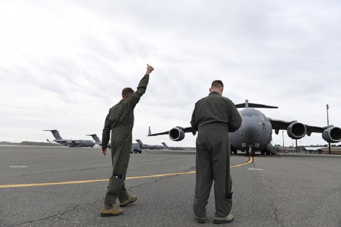 Two North Carolina Air National Guard Pilots walk towards a C-17 Globemaster III Aircraft. The pilot on the left is raising his hand and giving a thumbs up as part of the pre flight checks. 