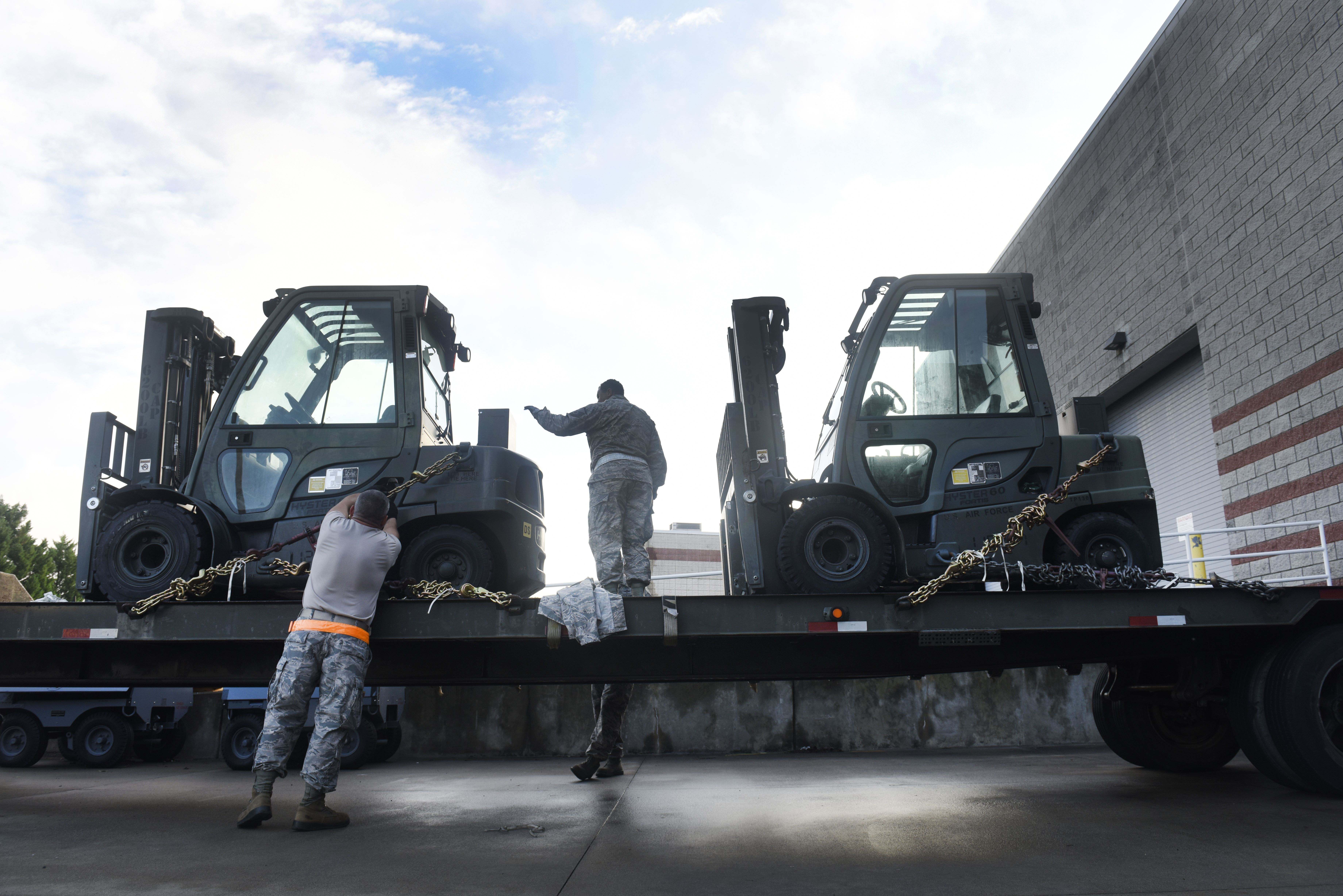 Photo of the 145th Logistics Readiness Squadron loading and securing two forklifts onto a flat bed truck. 