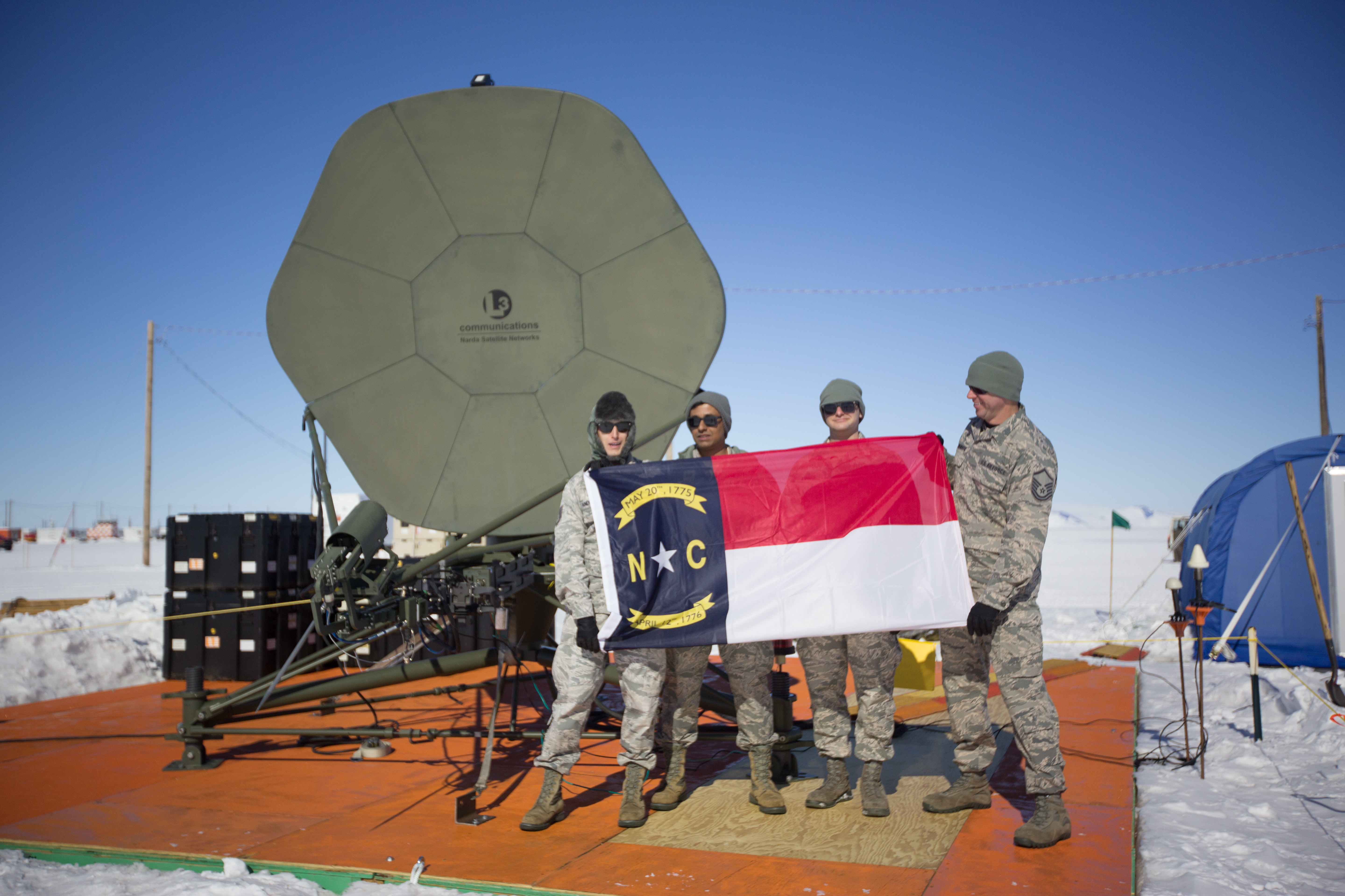 Photo of the 235th CCBS standing in front of a satellite holding the North Carolina Flag while in Antarctica. 