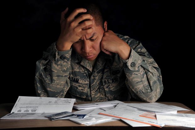 A photo of an Airman in ABUS's looking at frustrated at financial documents on his desk. 